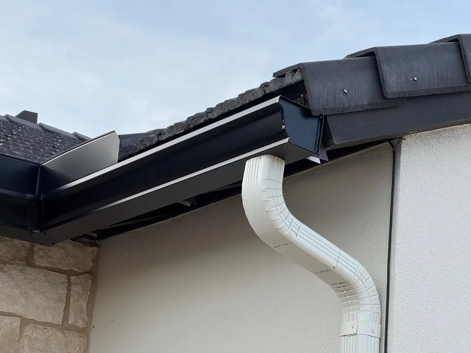 A 6-inch seamless dark bronze aluminum gutter with a white downspout on a stone and stucco Phoenix home, installed by Blueberry Gutters
