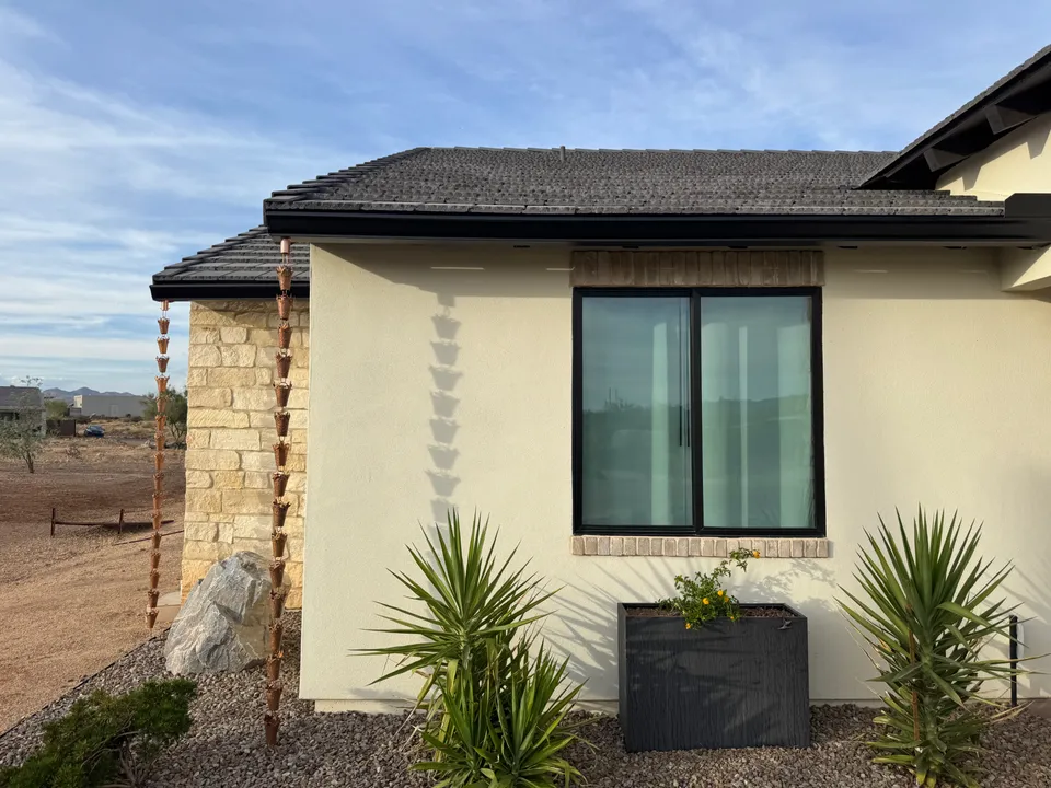Copper rain chains hanging from the roof edge of a tan stucco home