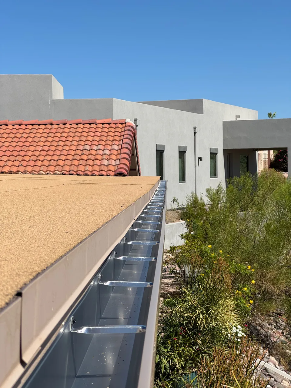 Mesh gutter guard installed along a seamless gutter on a tile roof