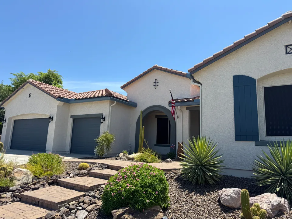 New gutters and a downspout at the front entry of a stucco home with desert landscaping