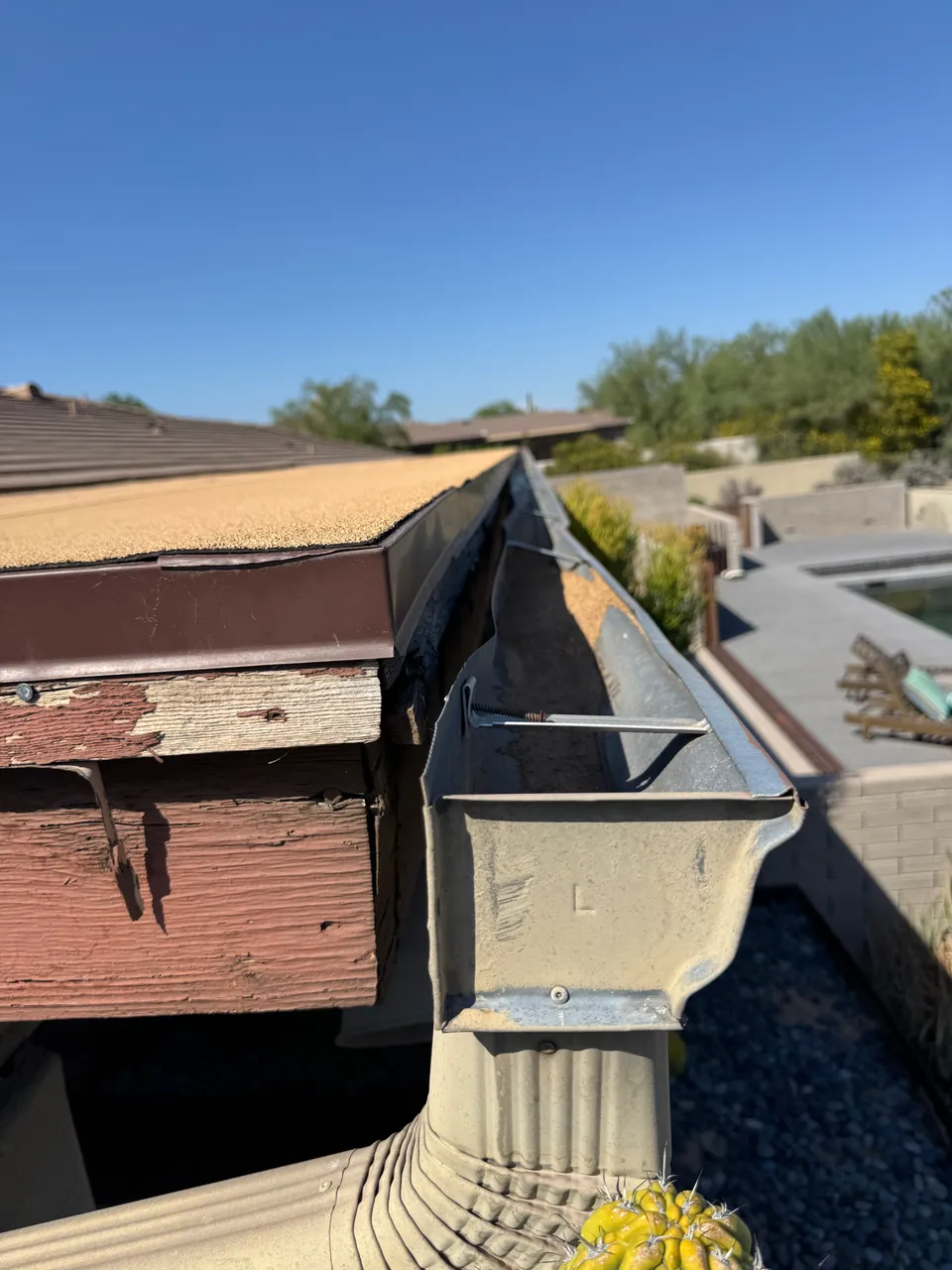 An old rusted sectional gutter full of debris on a Phoenix roof edge before repair