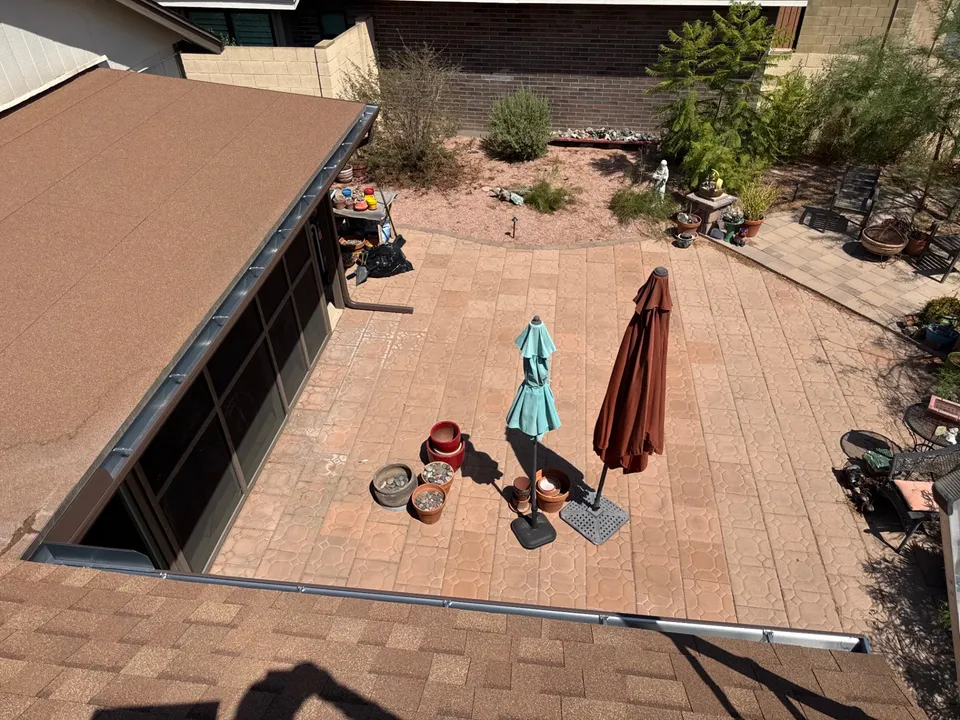 A paver patio directly below a roof edge with no gutter, seen from the roof