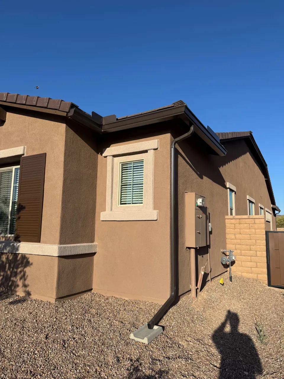 A brown stucco home with new seamless gutters and downspouts against a desert sky