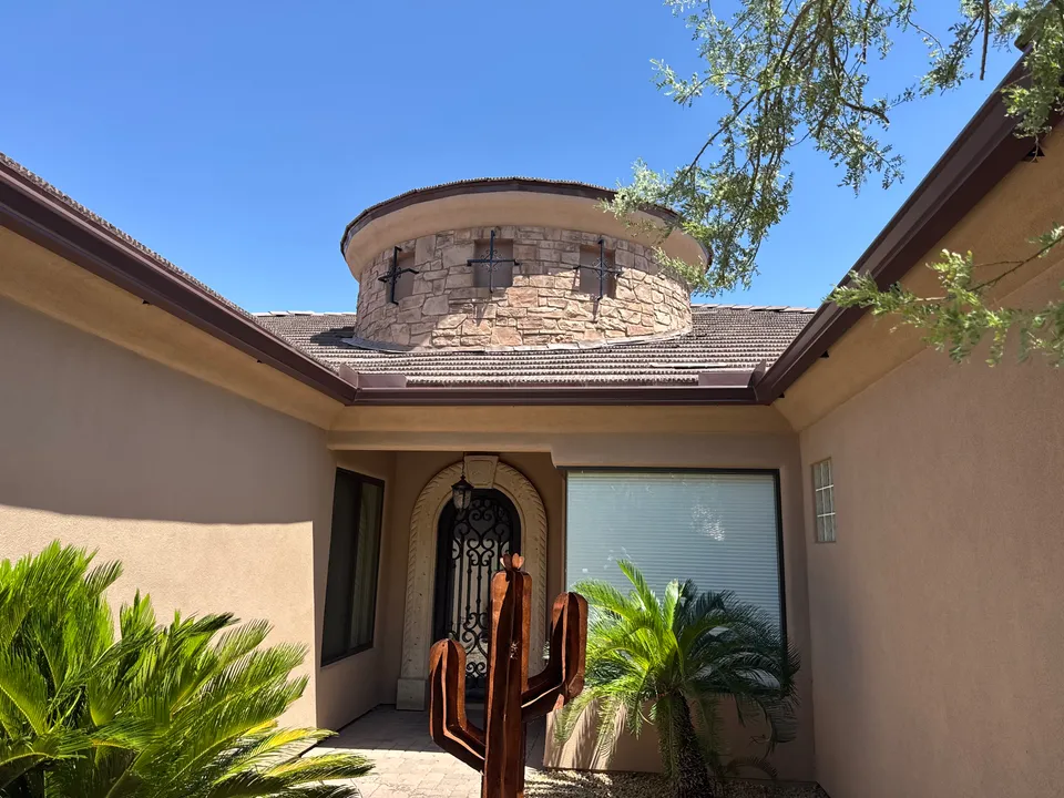 Seamless gutters along the roofline of a stucco home with a stone turret entry